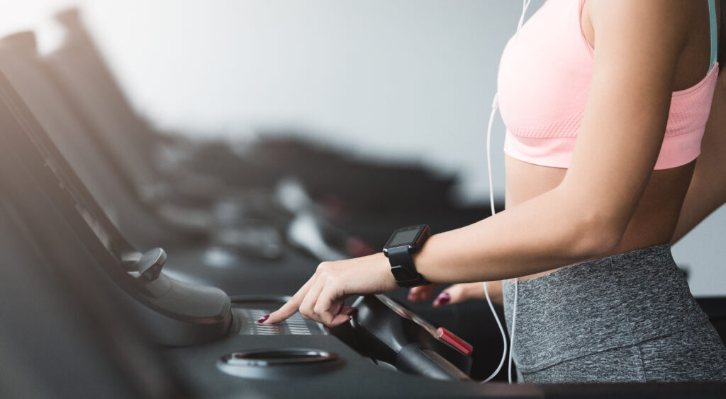 Girl adjusting speed on treadmill, doing cardio workout at YM&YEAH