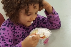 Little girl wearing purple dress eating Shavuot at YM&ДА